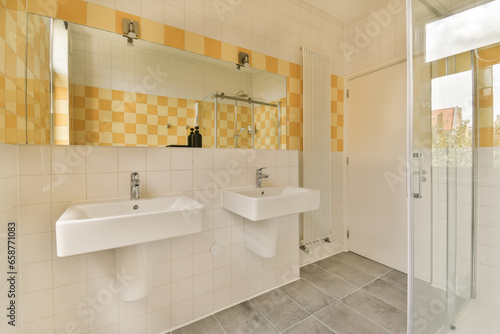 a bathroom with yellow and white tiles on the walls, two sinks and a shower stall in front of it