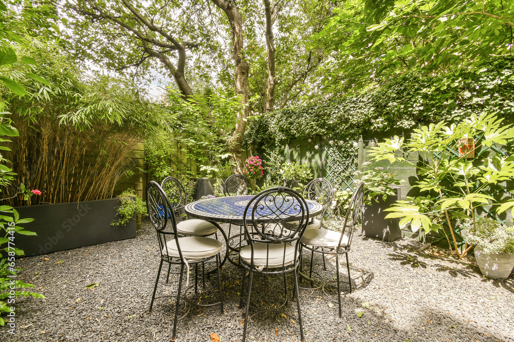 a table and chairs in a backyard setting with trees, plants, and flowers on the side wall behind it