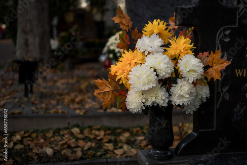 Vászonkép Autumn flower bouquet on a grave covered with fallen dry leaves in a cemetery