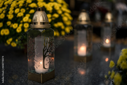 Lit grave candles among flowers on a grave at dusk — Poland, November 1, All Saints’ Day (also known as All Souls’ Day / Day of the Dead) decorations on the graves at evening