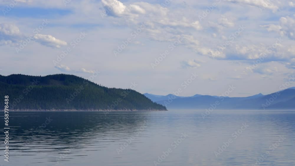 Establishing shot of Mountain lake with blue sky and white clouds in Vancouver, Canada, North America. Day time on July 2023. Still camera view. ProRes 422 HQ. Upper Arrow Lake. Establishing shot of Mountain lake with blue sky and white clouds in Vancouver, Canada, North America. Day time on July 2023. Still camera view. ProRes 422 HQ. Upper Arrow Lake.