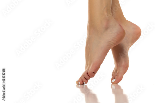 Elegant women's bare feet are showcased from a side view, highlighting their grace and beauty. Clpse up on white background.