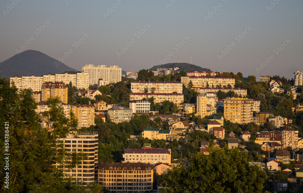 Sochi, Krasnodar Krai, Russia - August, 7, 2023: panoramic view of residential buildings among green hills in the city center at sunset and space for copying