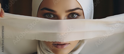 Young woman indoors wearing a white hijab presenting a paper with the words we the women in front of her face With copyspace for text photo