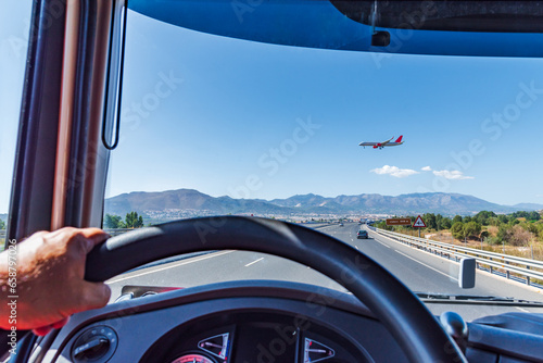 View from the driving position of a truck on a highway where a passenger plane prepared to land crosses, flying at low altitude.