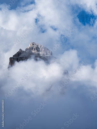 The peak of a rocky mountain in the dark illuminated by sunlight through the clouds, Dolomites, Italy
