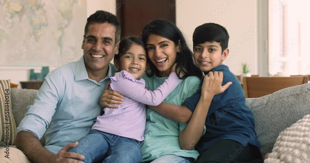 Beautiful Indian spouses posing for camera at home with their adorable little children, sit on couch at home smile staring at cam enjoy friendly relationships and understanding. Upbringing, adoption Beautiful Indian spouses posing for camera at home with their adorable little children, sit on couch at home smile staring at cam enjoy friendly relationships and understanding. Upbringing, adoption