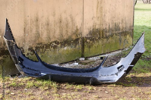 A plastic damaged bumper of a passenger car discarded next to a garbage can