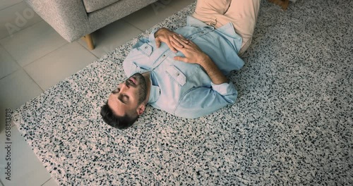 Above view of young upset Hispanic guy lying on carpet in cozy living room, feeling uncertain, thinking about unpleasant life situation, looking lonely, lazy or unmotivated spend time alone at home photo