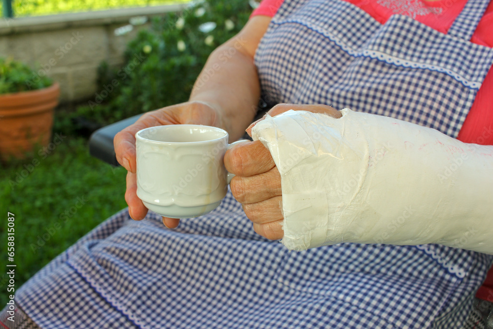 old woman with a cup of coffee in her hands, one of them with a cast old woman with a cup of coffee in her hands, one of them with a cast