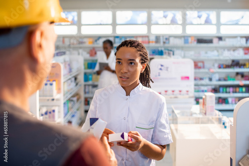 Young pharmacist offering advice to a construction worker about medication at the pharmacy photo