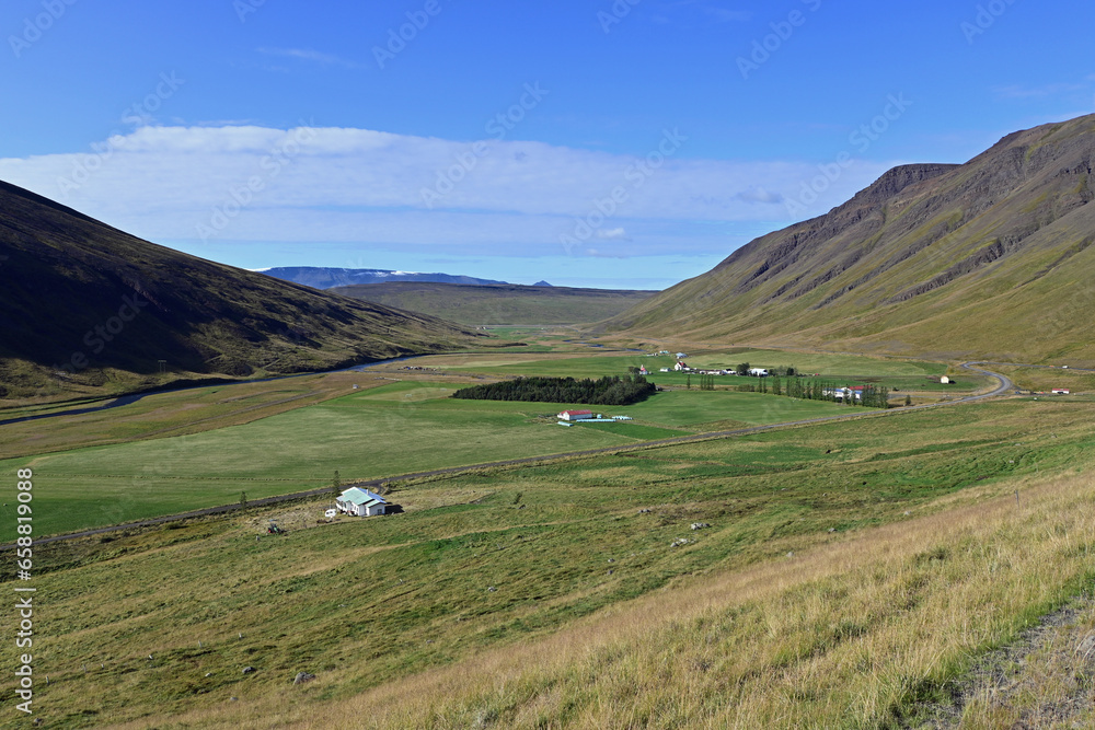 Sheep farm in green valley between volcanic mountains on Ring Road under clear blue sunny autumn sky in Iceland.