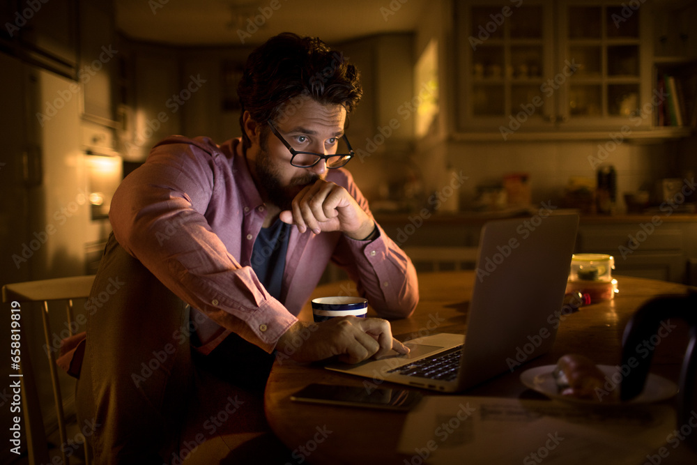 Stressed young man going over his bank balance on the laptop in the kitchen