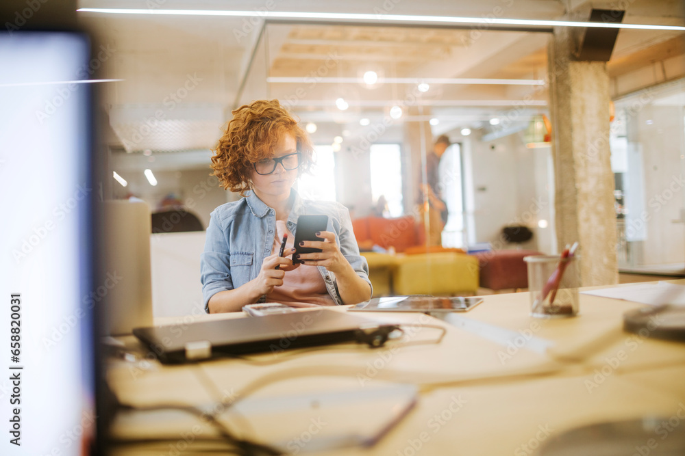 Young Caucasian woman using a smartphone in the office of a startup company