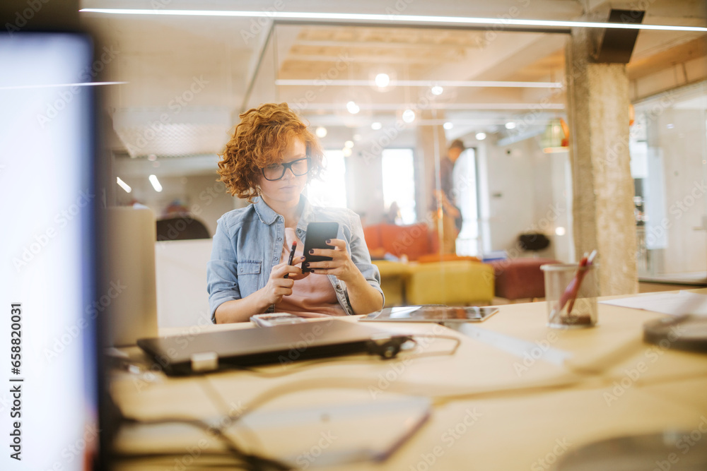 Young Caucasian woman using a smartphone in the office of a startup company Young Caucasian woman using a smartphone in the office of a startup company