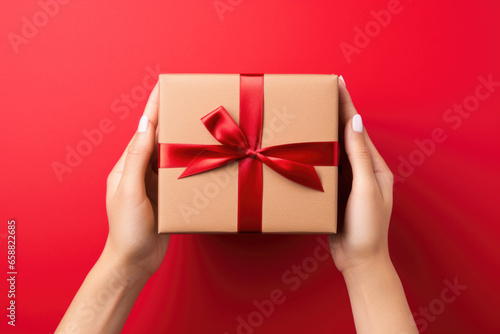 Women's hands holding gift box with red ribbon. © Maria