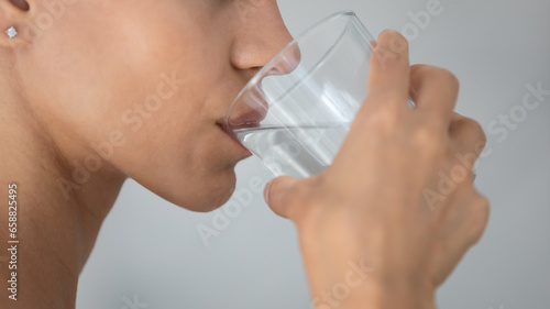 Close up side view of young woman drink clean mineral water from glass in home bath, millennial girl feel thirsty enjoy clear pure aqua after shower in bathroom, hydration, diet, wellness concept