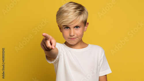 Young kid wearing a white tshirt mockup against a yellow background pointing his finger. T-shirt design template, print, mock-up © Mystikal Forest