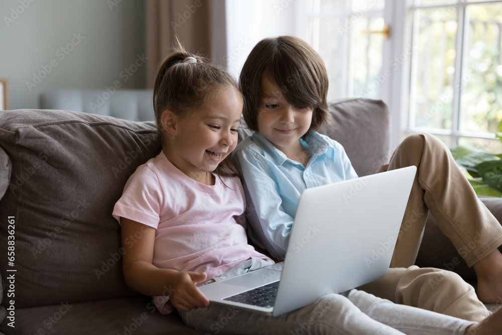 Two happy cute preschool sibling kids talking on video call on laptop, playing online virtual game, watching cartoon movie on Internet, enjoying wireless technology, communication, leisure Two happy cute preschool sibling kids talking on video call on laptop, playing online virtual game, watching cartoon movie on Internet, enjoying wireless technology, communication, leisure