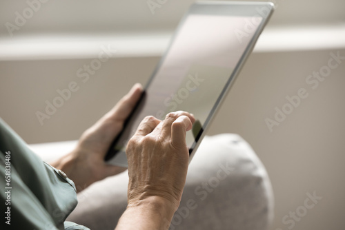 Hands of mature woman holding tablet computer, touching screen with finger, using online application, service on Internet, modern technology, wireless connection. Cropped close up shot
