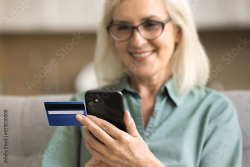 Close up of smartphone and credit card in female hands. Happy senior lady using financial commercial application, online banking service, shopping on Internet on mobile phone. Cropped shot