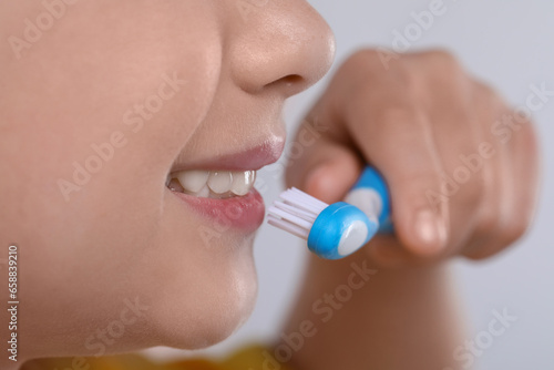 Girl brushing her teeth with toothbrush on light grey background, closeup