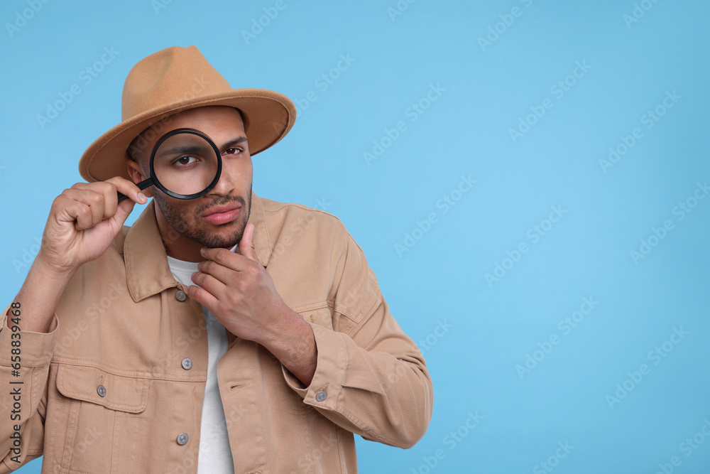 Curious man looking through magnifier glass on light blue background, space for text Curious man looking through magnifier glass on light blue background, space for text