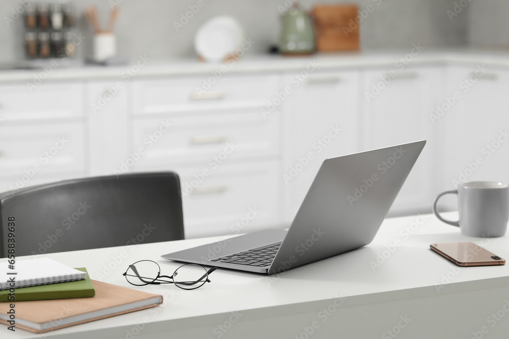 Home office. Laptop, glasses, smartphone and stationery on white desk in kitchen Home office. Laptop, glasses, smartphone and stationery on white desk in kitchen