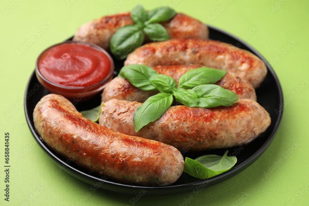 Plate with tasty homemade sausages, ketchup and basil leaves on green table, closeup