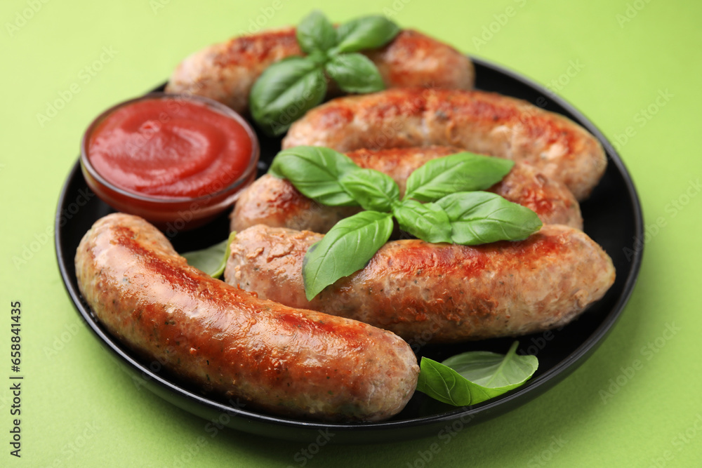 Plate with tasty homemade sausages, ketchup and basil leaves on green table, closeup Plate with tasty homemade sausages, ketchup and basil leaves on green table, closeup