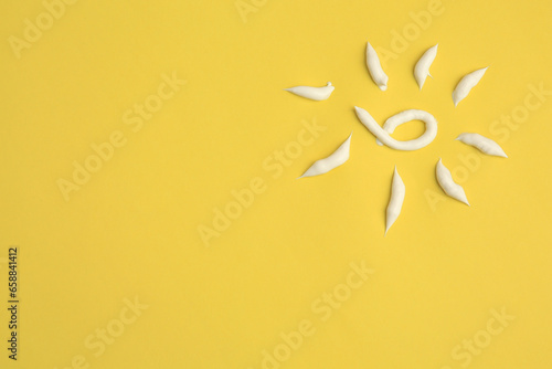 Drawing of sun with cream on yellow background  above view and space for text. Skin care and protection