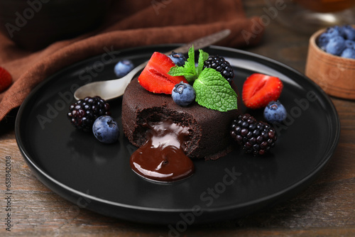 Plate with delicious chocolate fondant, berries and mint on wooden table, closeup