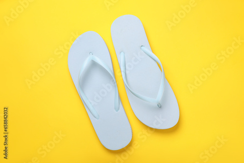 Stylish white flip flops on yellow background, top view