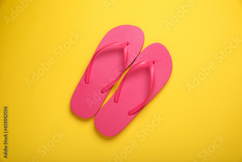 Stylish pink flip flops on yellow background, top view