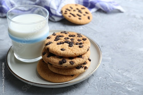 Delicious chocolate chip cookies and glass of milk on grey textured table  space for text