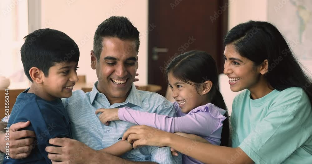 Beautiful loving Indian parents posing for camera with cute little son and daughter, tickling each other feel happy enjoy playful mood and time together sit on couch at home. Wellbeing family portrait Beautiful loving Indian parents posing for camera with cute little son and daughter, tickling each other feel happy enjoy playful mood and time together sit on couch at home. Wellbeing family portrait