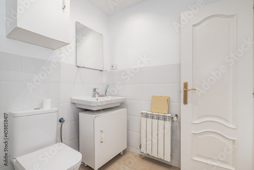 Bathroom with small white porcelain sink under a suspended mirror  white aluminum radiator and white square furniture