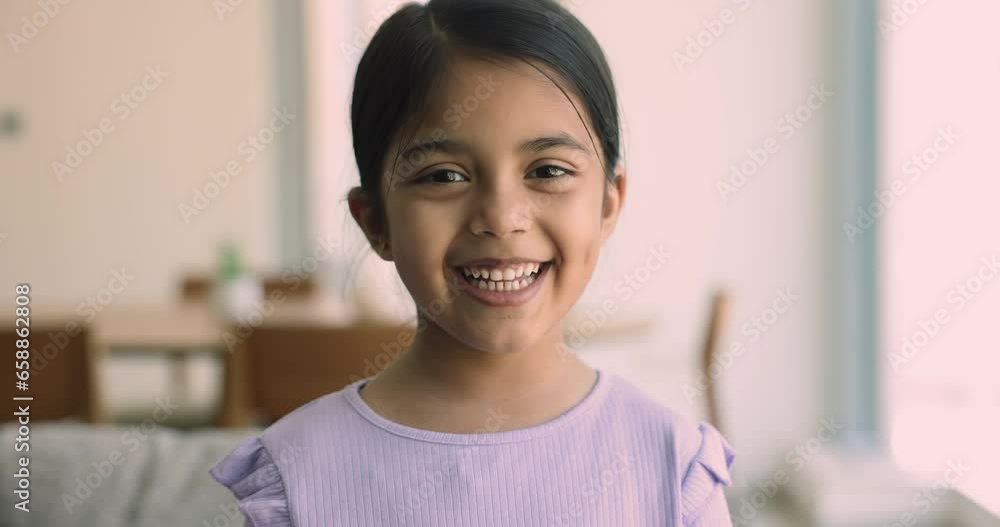 Close up head shot of preschooler Indian girl sitting alone on couch at home smile looking at camera, feel happy and satisfied. Carefree childhood, portrait of candid, beautiful, Alpha generation kid Close up head shot of preschooler Indian girl sitting alone on couch at home smile looking at camera, feel happy and satisfied. Carefree childhood, portrait of candid, beautiful, Alpha generation kid