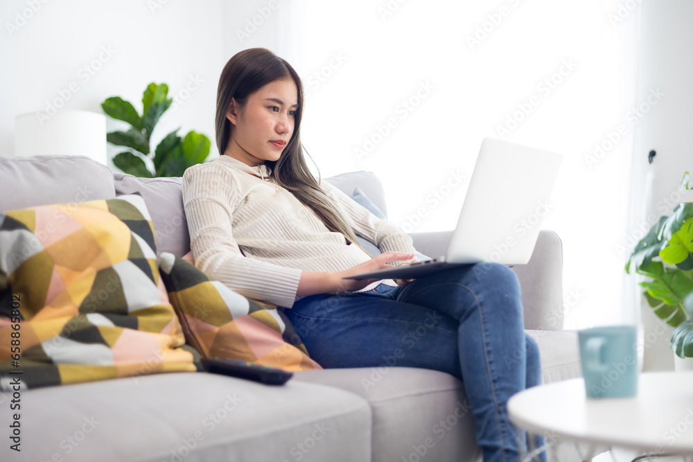 Naklejka premium Reading email and working. Asian thai young woman sitting working on laptop computer. Wellness at home