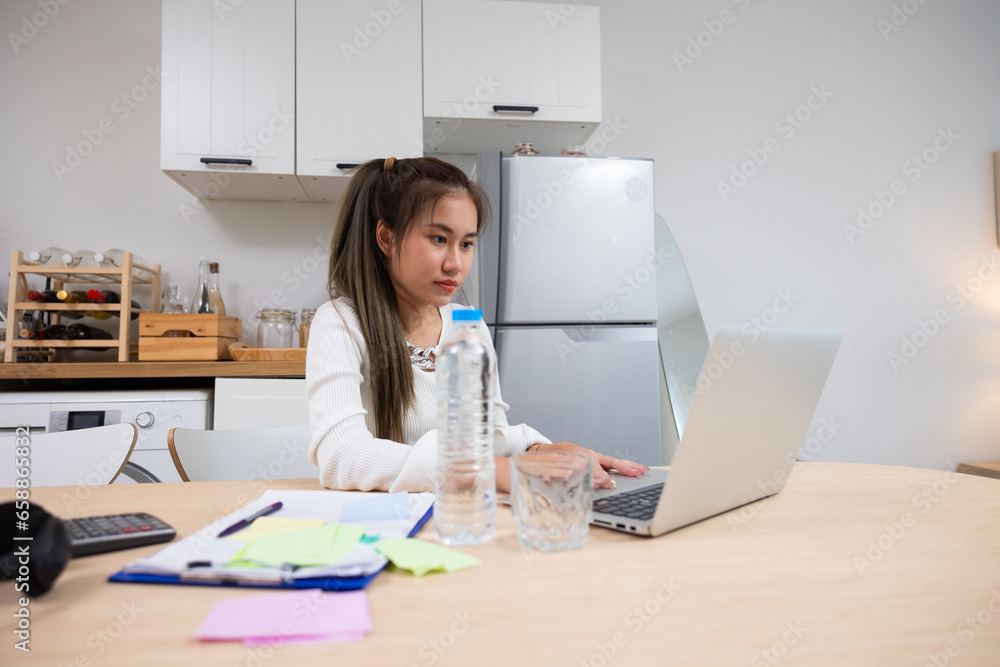 Thai Asian Woman working on laptop computer and opening plastic bottle of water at home office. searching information online, working from home Thai Asian Woman working on laptop computer and opening plastic bottle of water at home office. searching information online, working from home