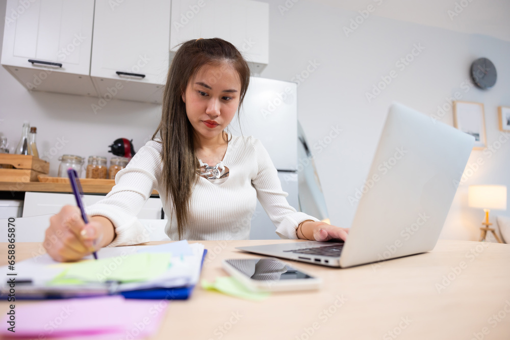 writing note or journal on note book. Reading email and working. Asian thai young woman sitting working on laptop computer. Thai female using laptop and smiling at home. writing note or journal on note book. Reading email and working. Asian thai young woman sitting working on laptop computer. Thai female using laptop and smiling at home.
