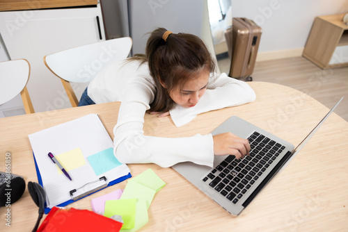 Tired exhausted, fatigue and fell asleep. Yaoung asian thai female working on laptop in kitchen room at home. Overwork. Exhausted woman  sleeply eye at workplace photo