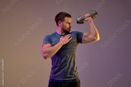 serious fit man performing weightlifting exercise. guy looks at his arm . isolated brown background.