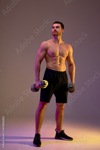 motivated talented bodybuilder posing to the camera, resting after workout, wellness, full length photo, isolated brown background, motivation, health and body care