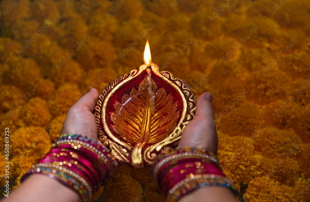 Female hands hold a clay diya lamps lit above marigold during diwali celebration,