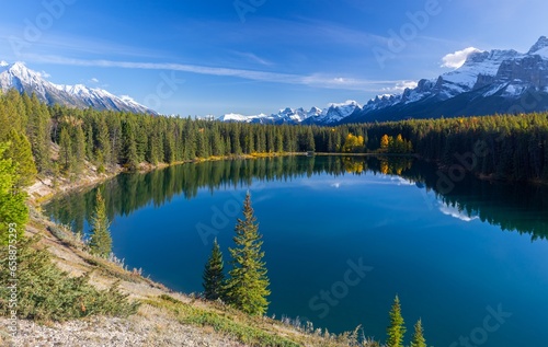 Fototapeta Naklejka Na Ścianę i Meble -  Treelined Shore Blue Rocky Mountain Lake, Scenic Autumn Landscape, Distant Snow Covered Peaks, Banff National Park, Canadian Rockies Alberta Foothills