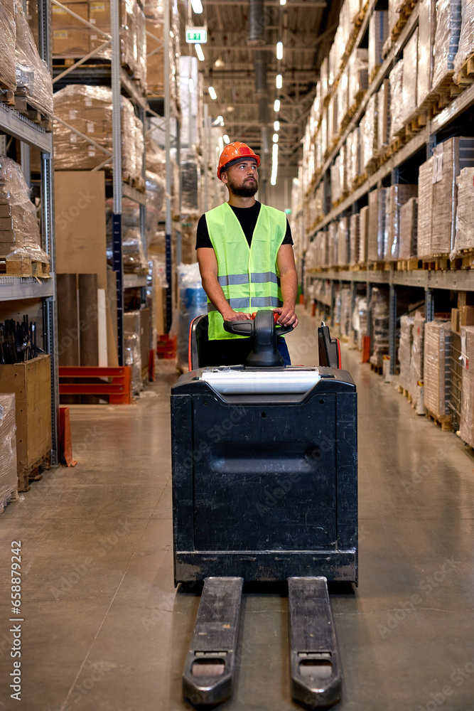 Forklift driver in warehouse. Road freight transport, Warehouse industrial delivery shipment, caucasian male pushing transport equipment, dressed in green uniform vest and safety helmet Forklift driver in warehouse. Road freight transport, Warehouse industrial delivery shipment, caucasian male pushing transport equipment, dressed in green uniform vest and safety helmet