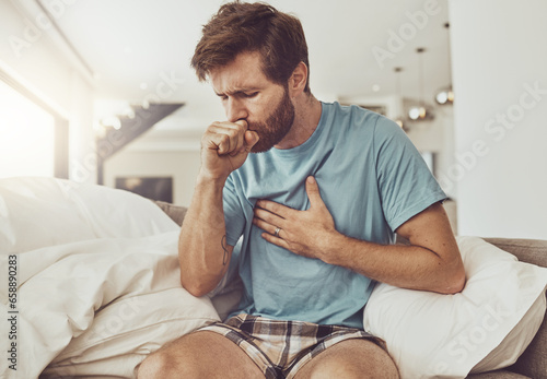 Sick, coughing and man on a sofa with chest pain, tuberculosis or influenza at home. Asthma, anxiety and male person with breathing trouble in living room with covid, pneumonia or lung virus photo