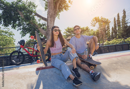 Young happy couple with skateboards enjoy longboarding at the skatepark photo