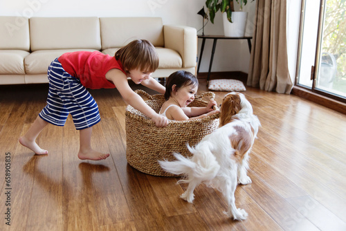 Happy siblings playing together in living room with their dog